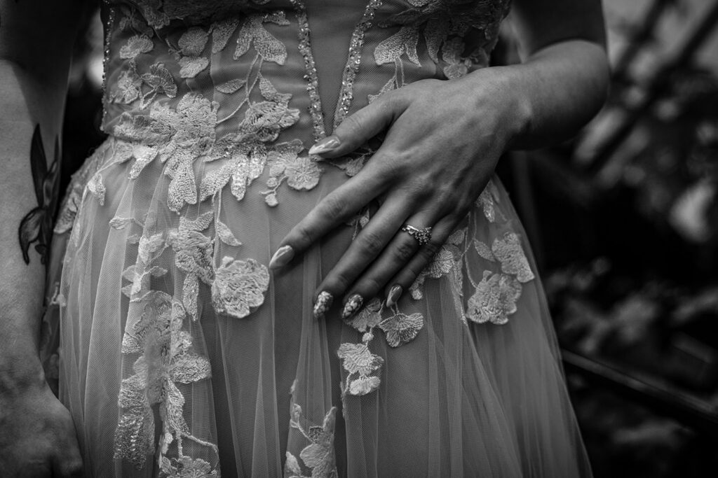 Black and white detail photo of the bride's hand resting on the front of her dress